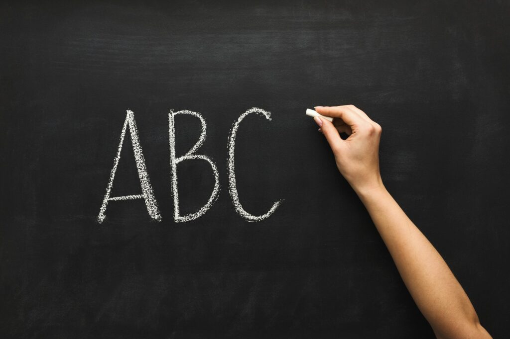 Woman writing abc on black chalkboard